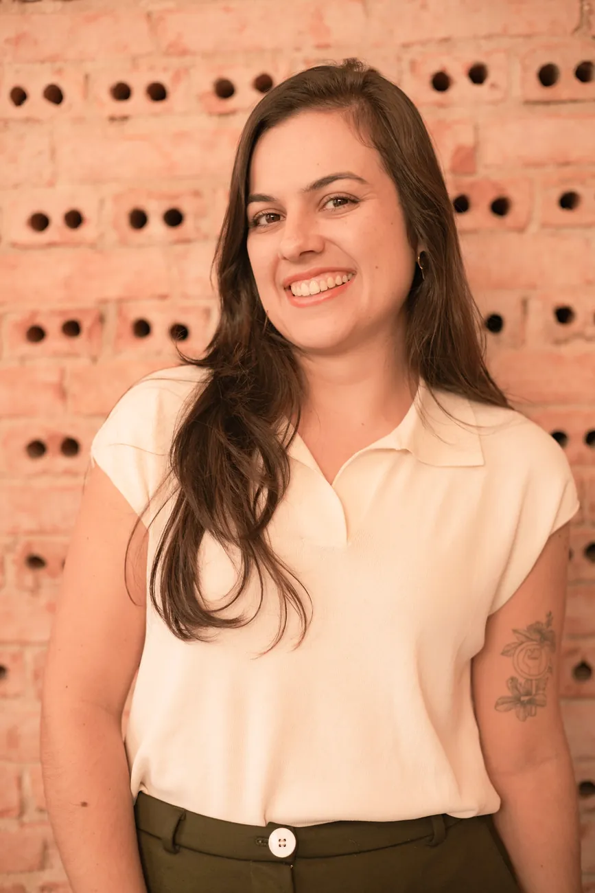Retrato da arquiteta Maria Luísa sorrindo, em frente a uma parede de tijolos aparentes